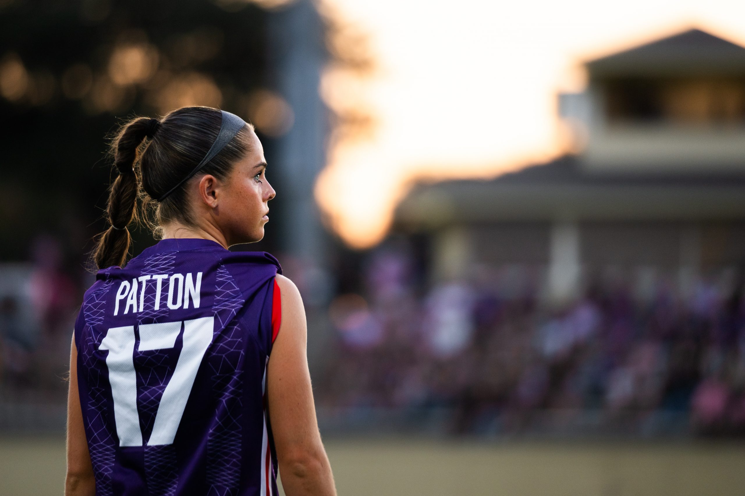 Cameron Patton looks over her shoulder in a purple TCU jersey at dusk, with spectators blurred in the stands behind her.