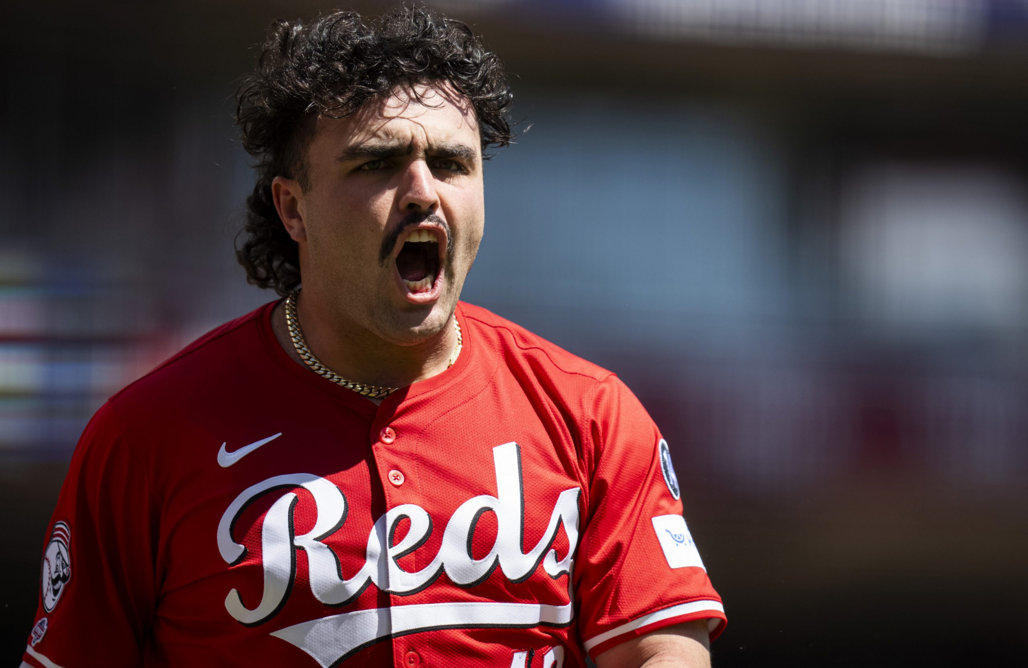 A Cincinnati Reds player in a red jersey shouts in celebration, shown in close-up with the background blurred.