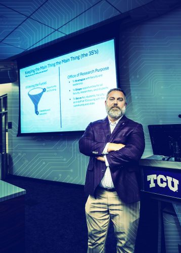 Reuben F. Burch V, in a purple blazer, checked shirt and khakis, stands with his arms crossed at the front of a TCU room. Behind him, a projection screen displays a slide titled ‘Keeping the Main Thing the Main Thing (the 3S’s),’ with a funnel diagram labeled ‘Widening the Funnel’ and a list of Office of Research purposes. A lectern with the TCU logo stands beside him, and a circuit board pattern runs across the wall behind.