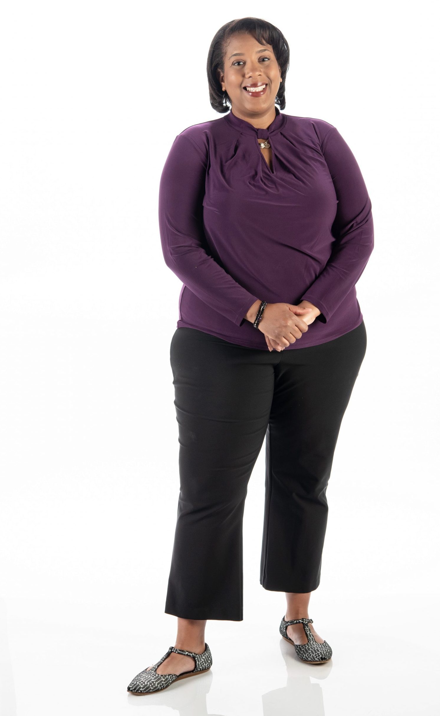 Karen Morgan, TCU dean of students, stands with her hands clasped and smiles in a purple top and black pants against a white studio backdrop.