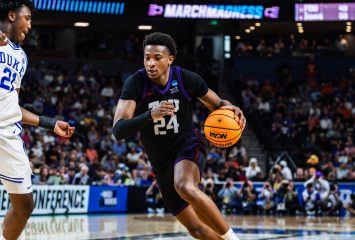 Xavier Edmonds, in a black TCU No. 24 jersey, drives with the ball past a defender in a white Duke uniform in front of a packed arena.