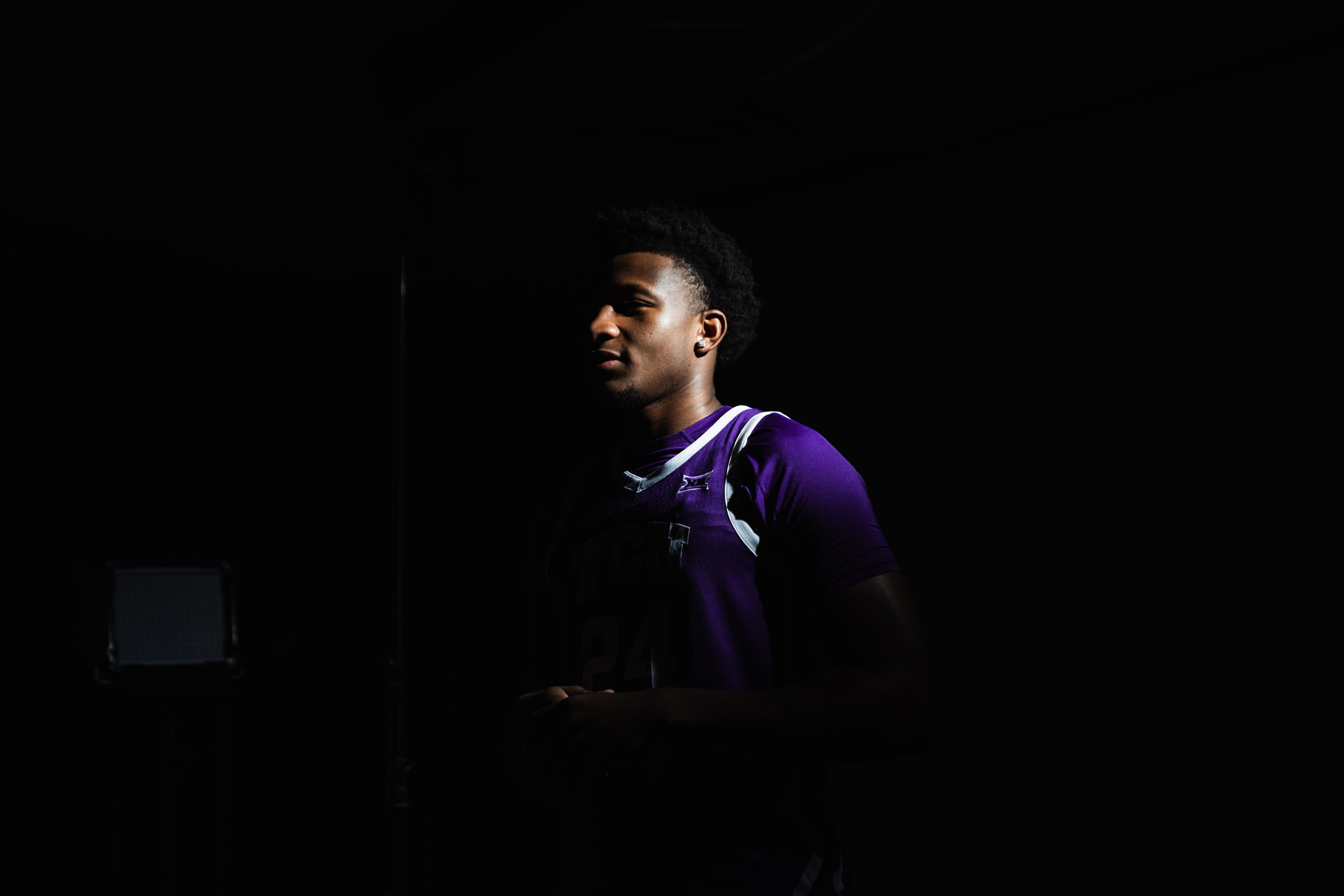 Xavier Edmonds, in a purple TCU No. 24 jersey, stands in shadow with light falling across his face and shoulder.